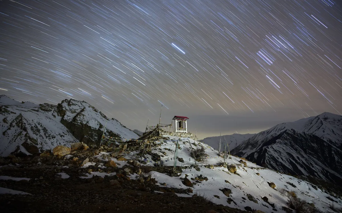 Star trails over snowy mountains and a small shrine