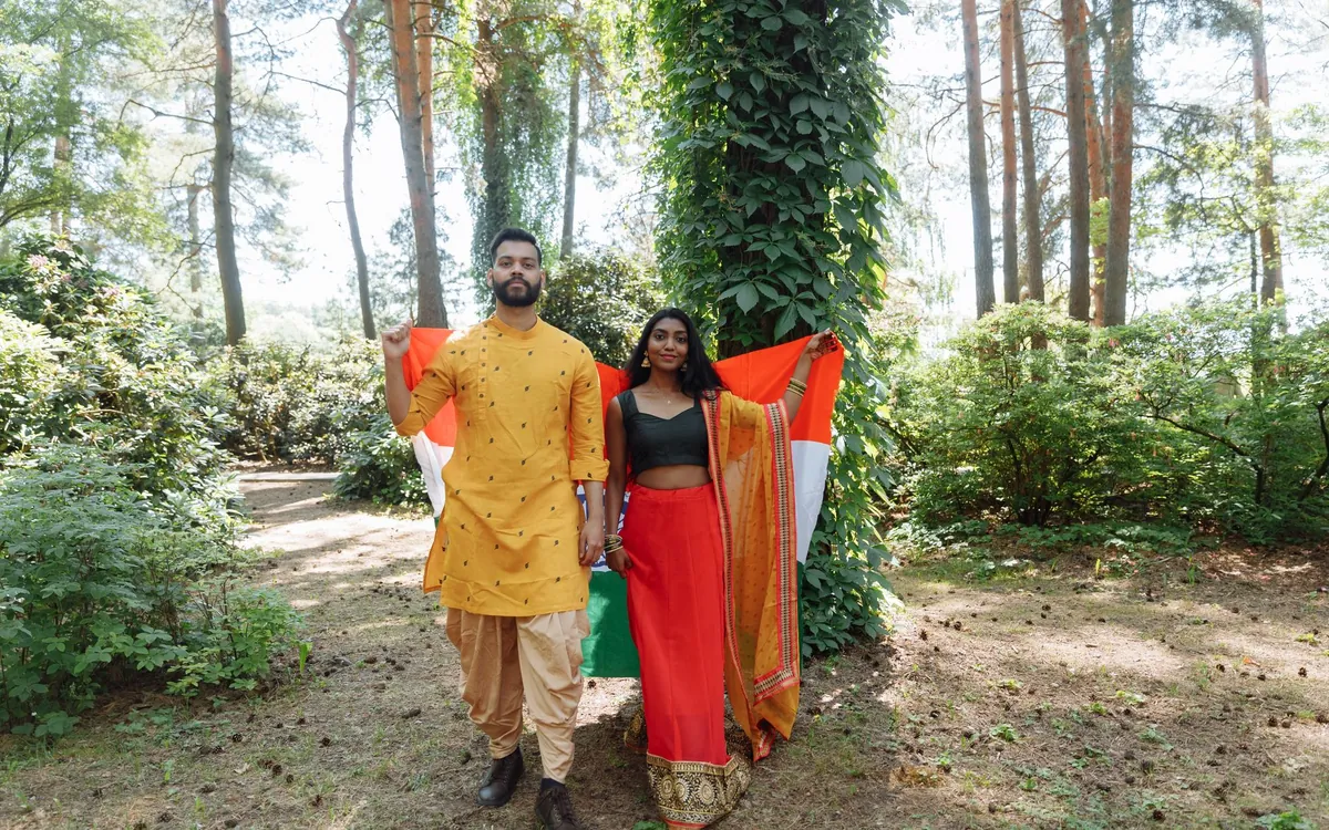 A couple in a yellow kurta and red saree walking in a forest