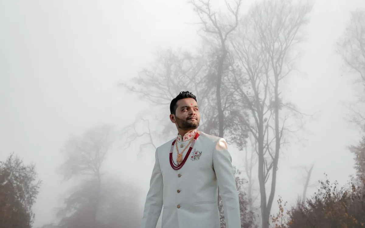 A groom in a sherwani standing on a foggy winter morning