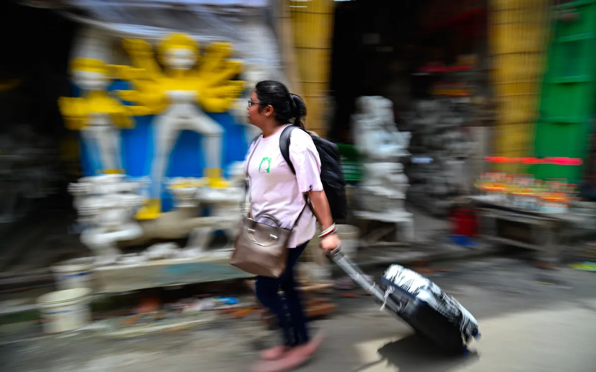 A young Indian woman pulling a suitcase through a city street