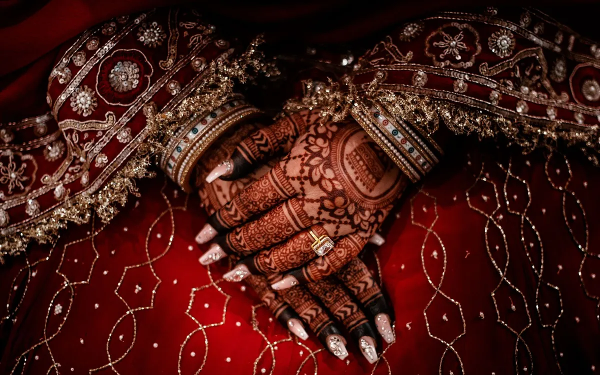 A bride's hennaed hands resting on a red embroidered lehenga
