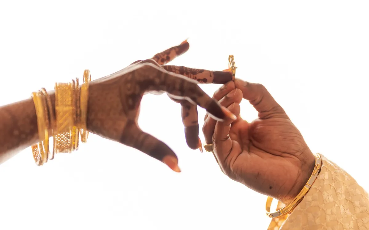 A man slipping a ring onto a woman's hennaed finger