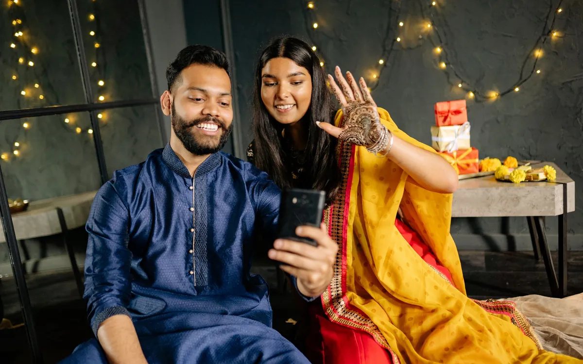 An Indian couple in festive clothes sitting together under fairy lights