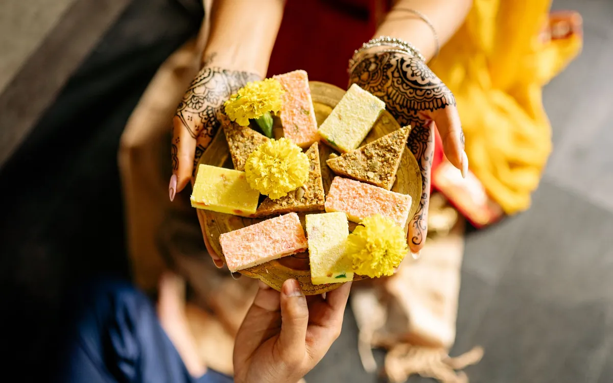 Hands holding a plate of Indian sweets decorated with marigold