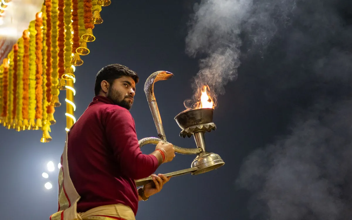 A man performing aarti with a brass lamp at a riverside ceremony