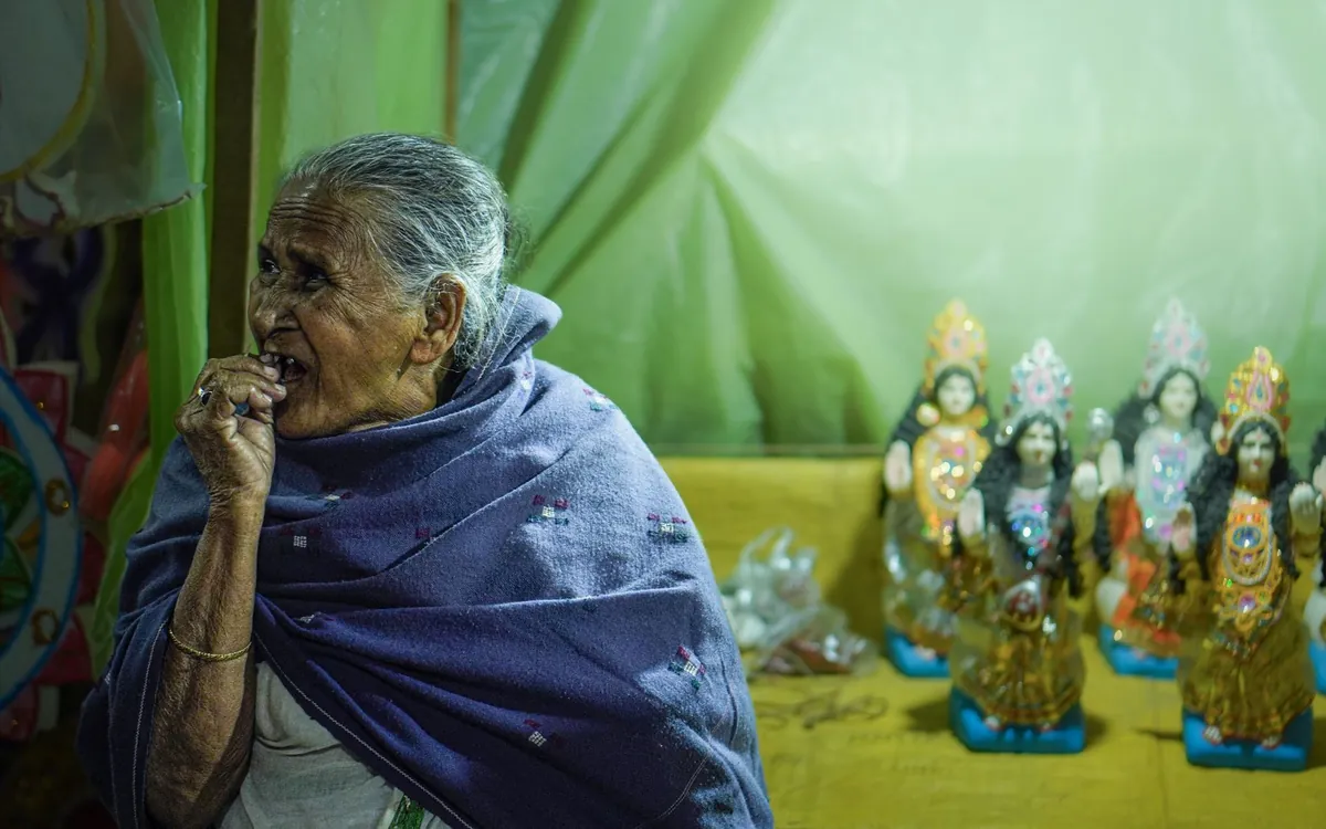 An elderly Indian woman beside small idols of Hindu deities