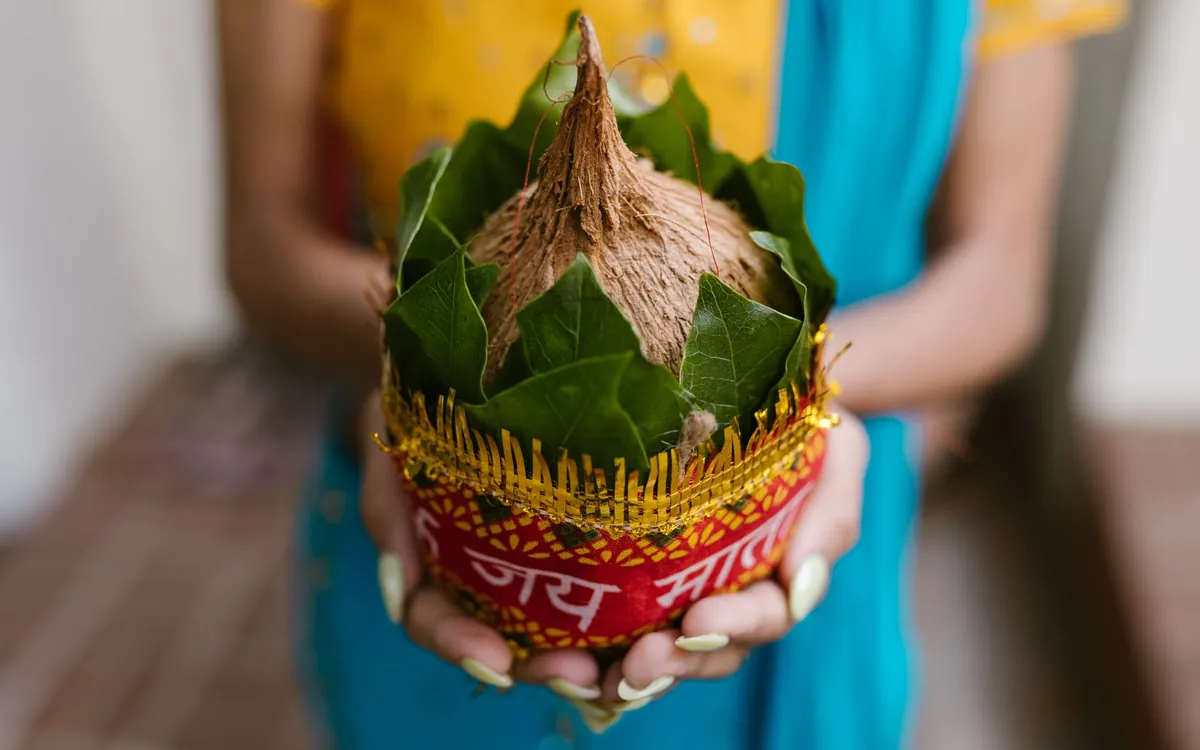 A decorated coconut on a kalash held in a woman's hands