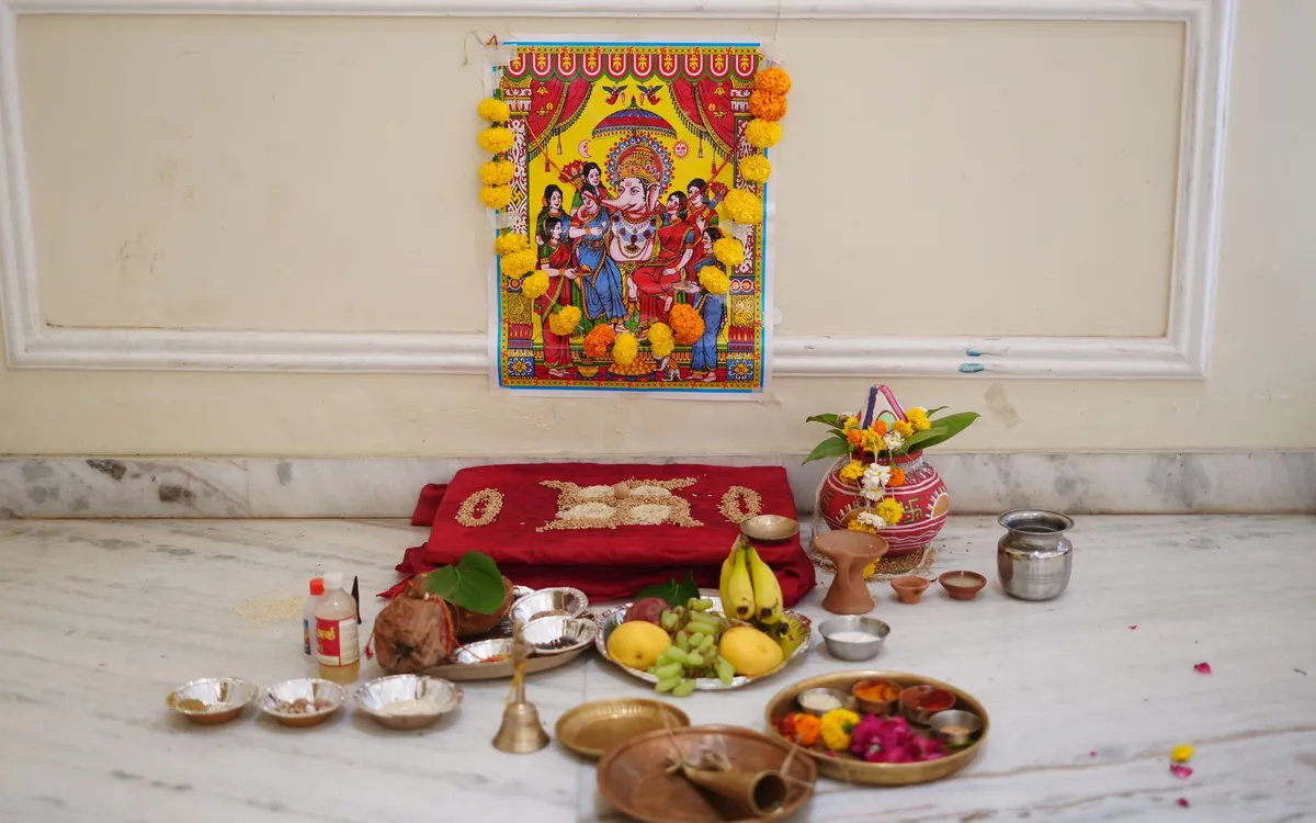 A home puja setup with brass lamps, fruits and a deity painting