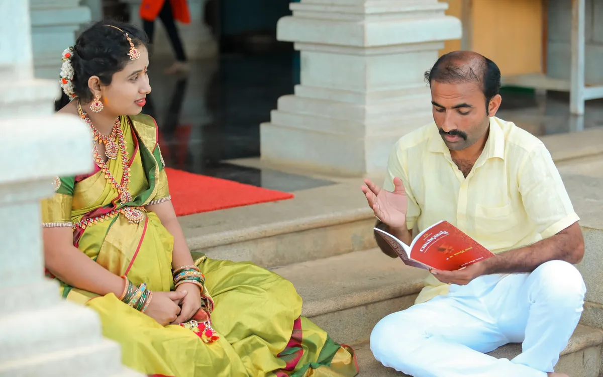 A young woman in a saree talking with an older man on temple steps