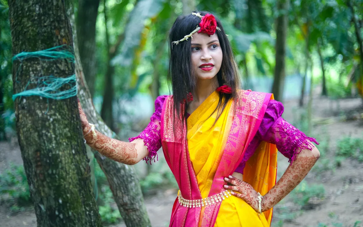 A young Indian woman in a bright saree standing among trees