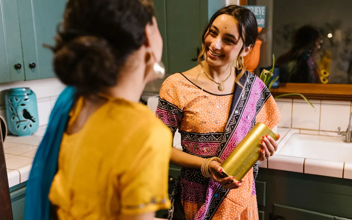 Two Indian women in sarees talking in a home kitchen