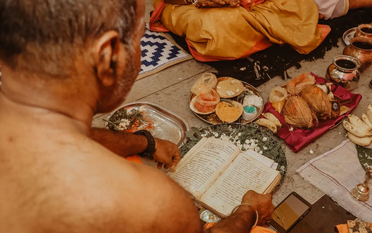 A Hindu priest's hands with a ritual book and puja items