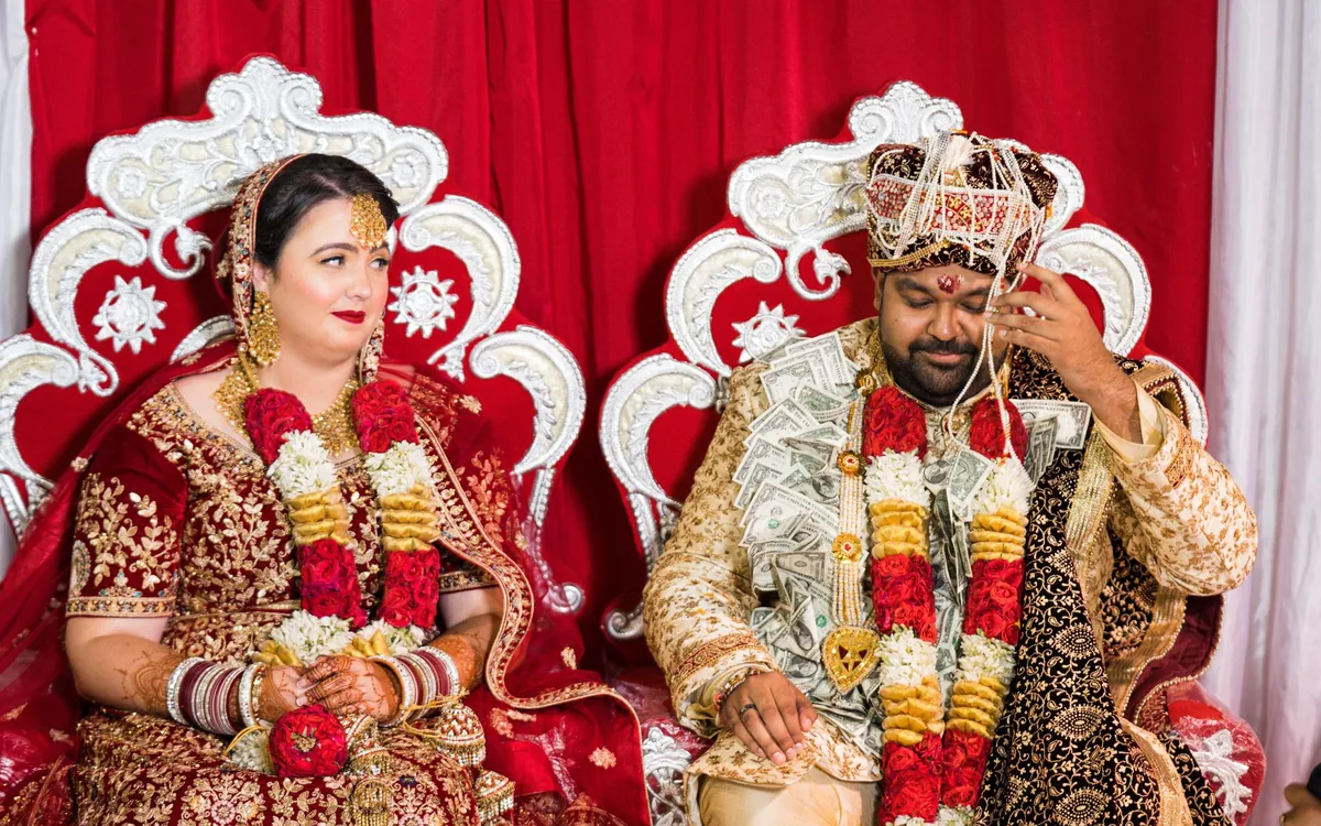 A newly married Indian couple seated on decorated chairs at their wedding