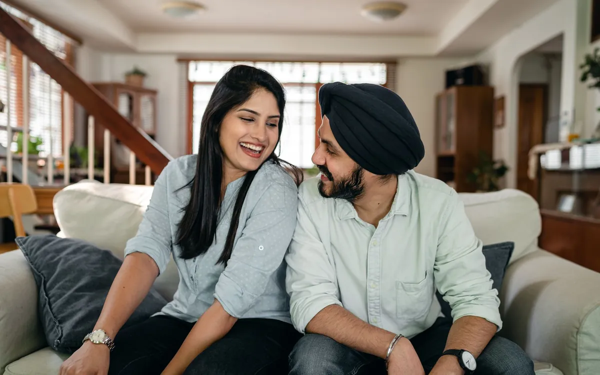A young Indian couple laughing together on a sofa at home