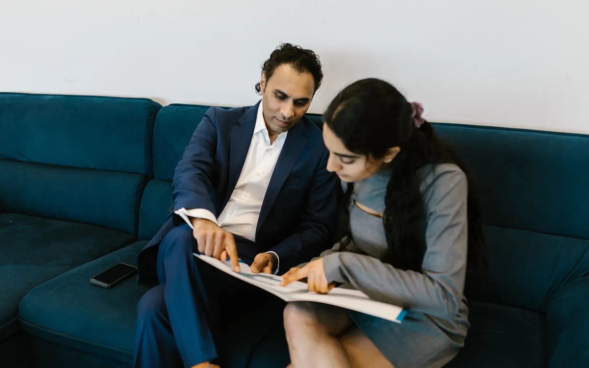 A man and woman in office clothes reading a document together on a sofa