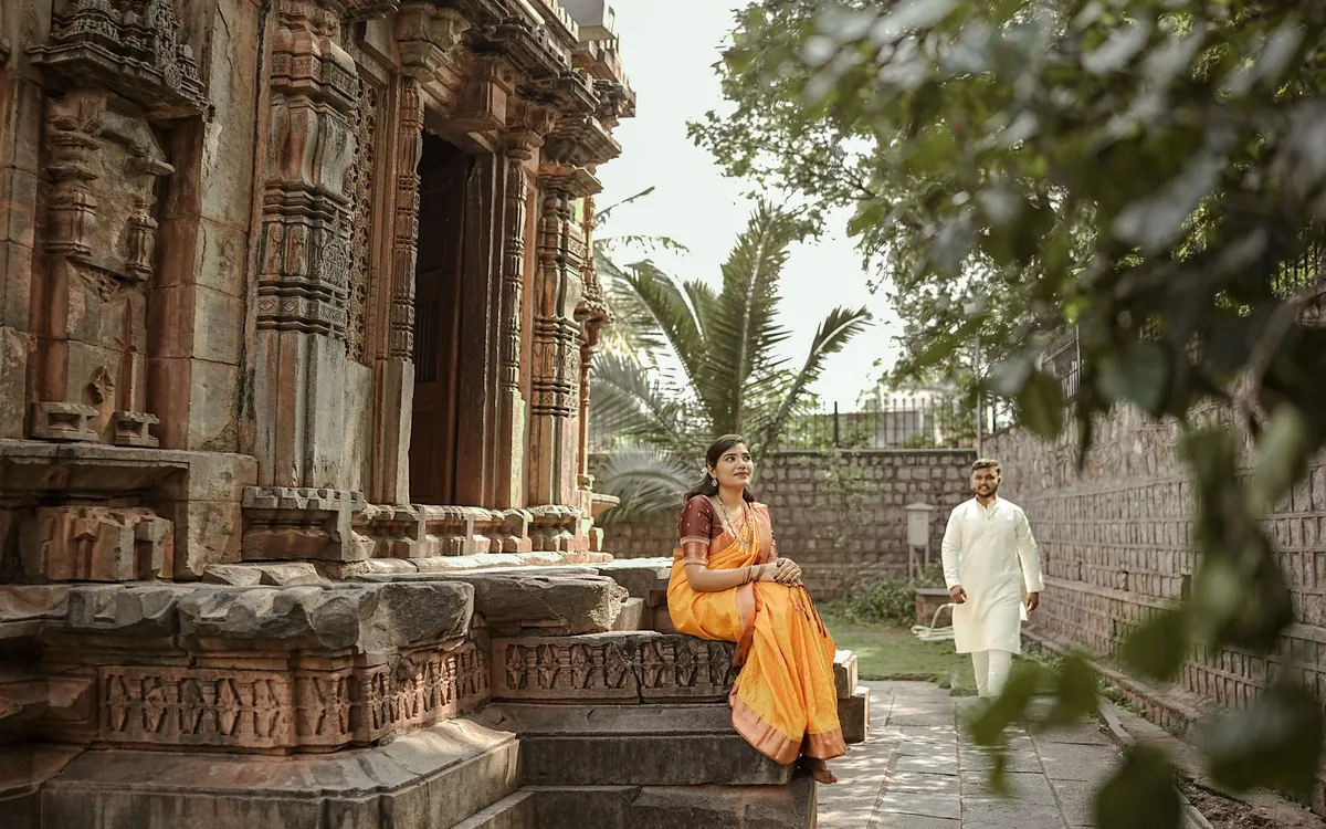 A woman in a yellow saree sitting by an old stone temple