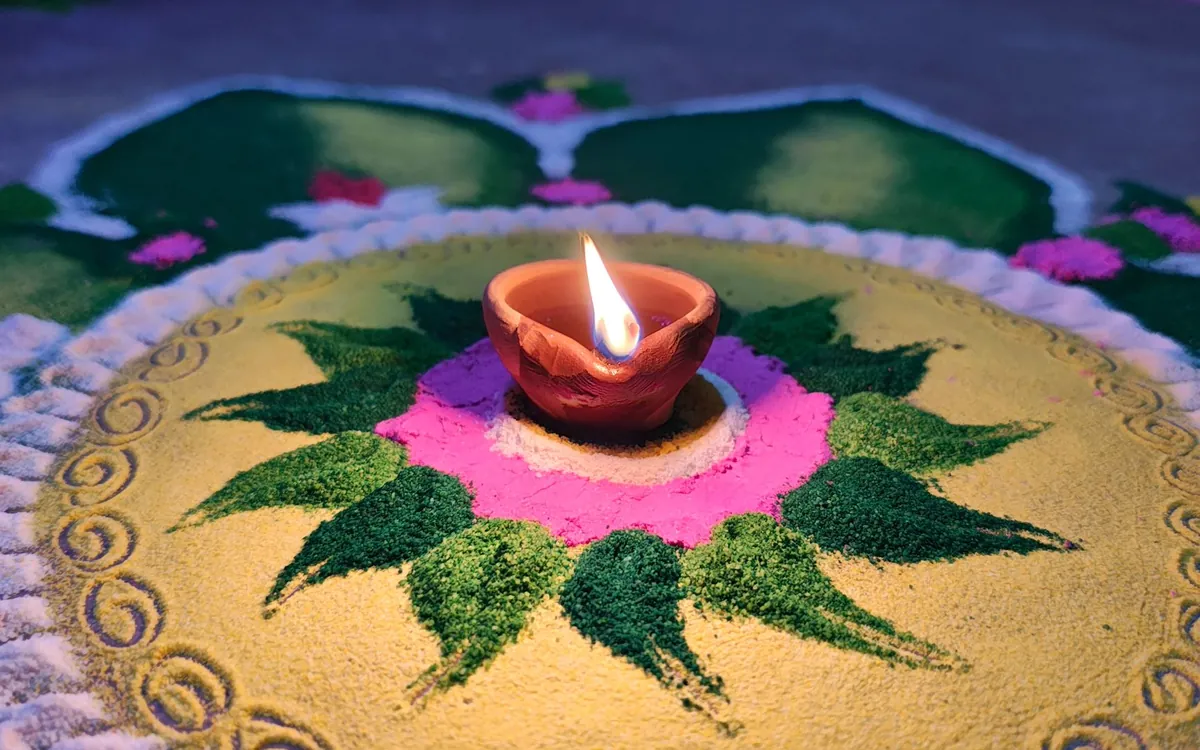 A diya burning at the centre of a colourful rangoli