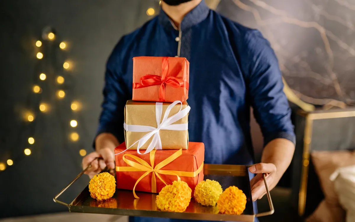 A man holding a tray of wrapped gift boxes and marigolds