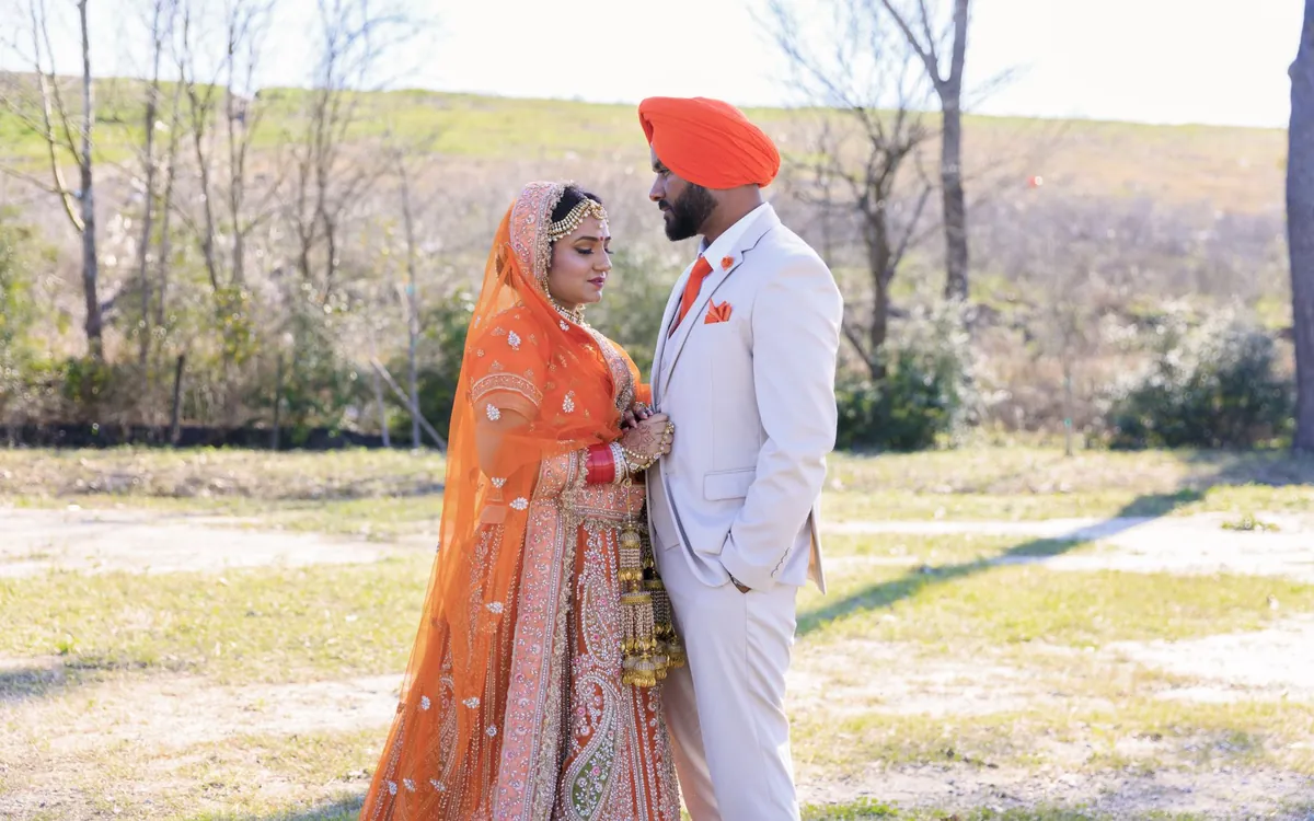 A bride in an orange lehenga and a groom in a turban standing in a field