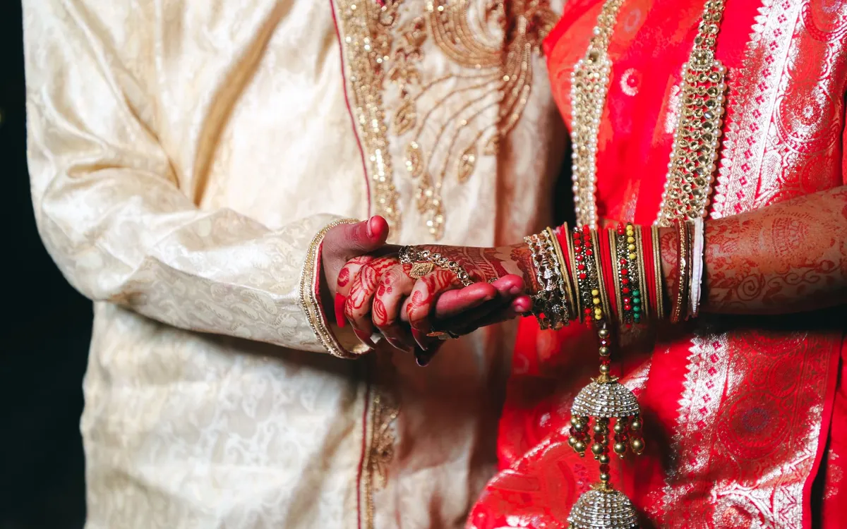 A couple's hands together, the bride wearing red bangles and mehndi